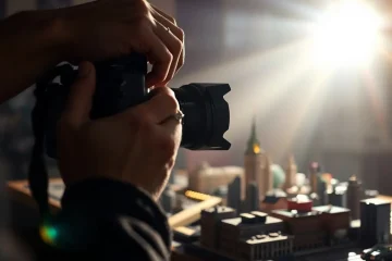 alt_text: A filmmaker adjusts lighting on a DSLR camera, focused on a detailed miniature cityscape with dramatic cinematic flair.